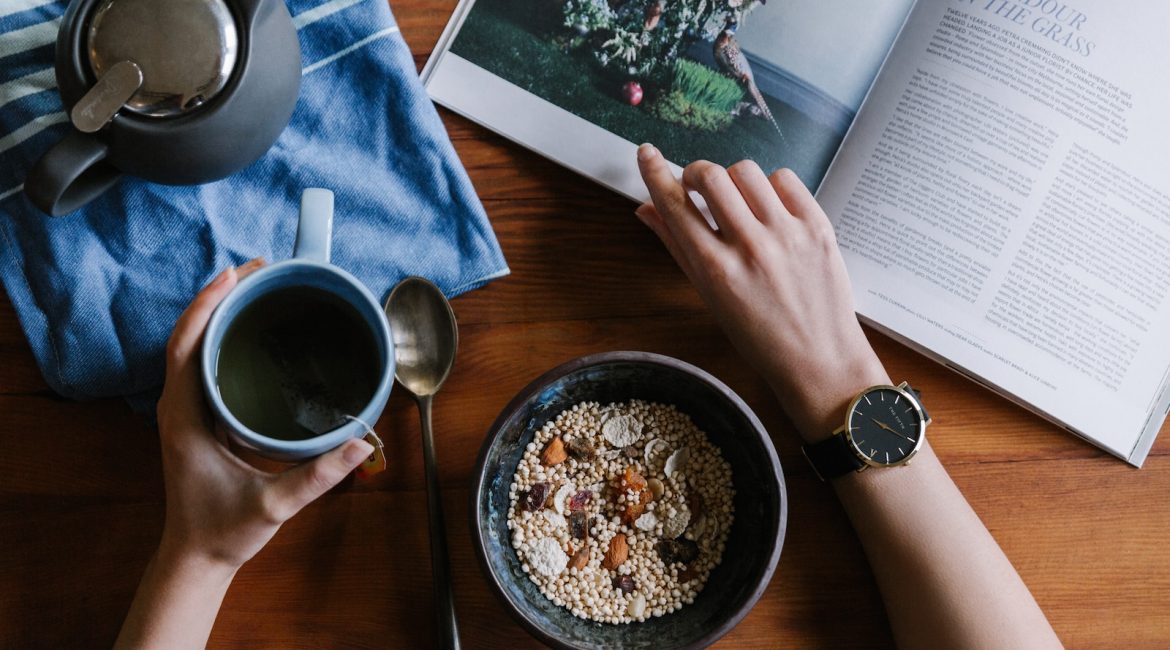 person holding blue ceramic mug and white magazine