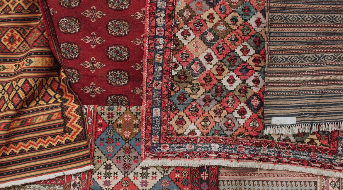 A close-up of various patterned rugs in rich red and earthy tones, with intricate designs