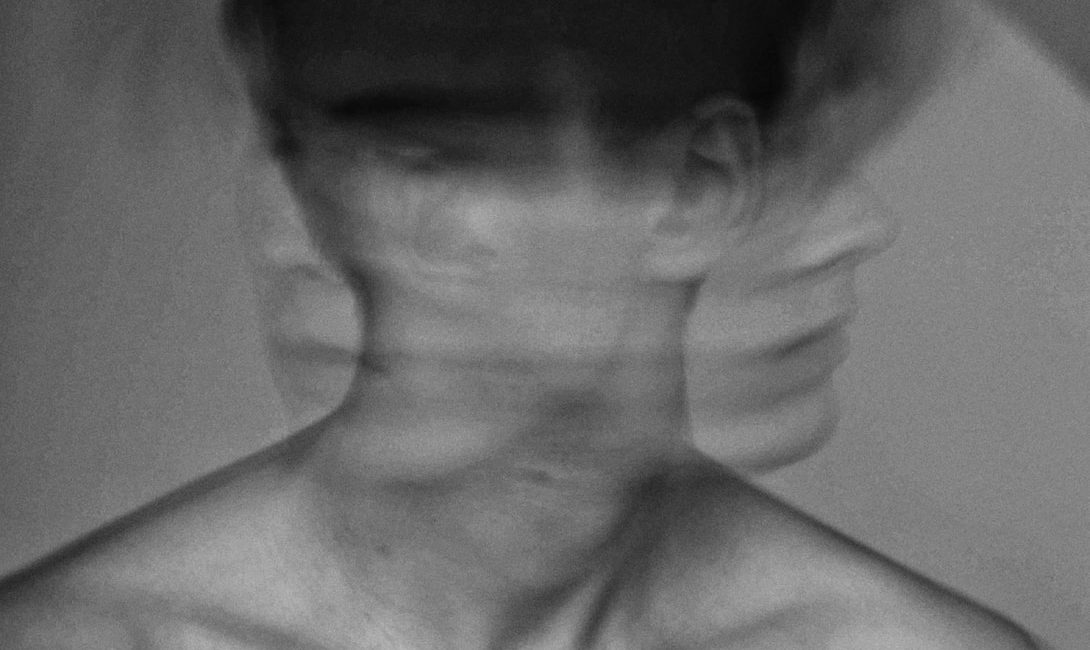 Black-and-white abstract portrait of a person with multiple overlapping faces, creating a motion blur effect