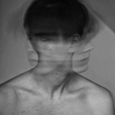 Black-and-white abstract portrait of a person with multiple overlapping faces, creating a motion blur effect