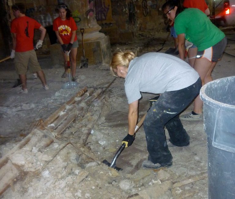 Group of people working together on a construction site, using tools to break up debris in a building under renovation