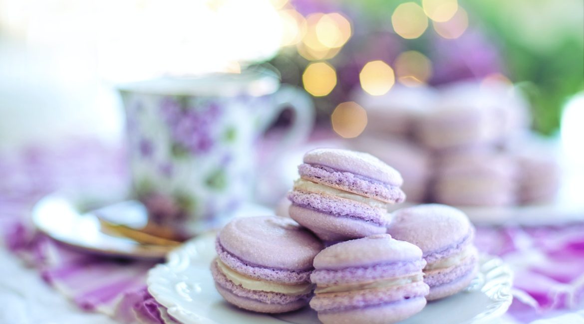 A plate of lavender macarons with a floral teacup in the background, creating a soft, elegant atmosphere