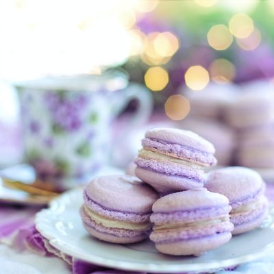 A plate of lavender macarons with a floral teacup in the background, creating a soft, elegant atmosphere