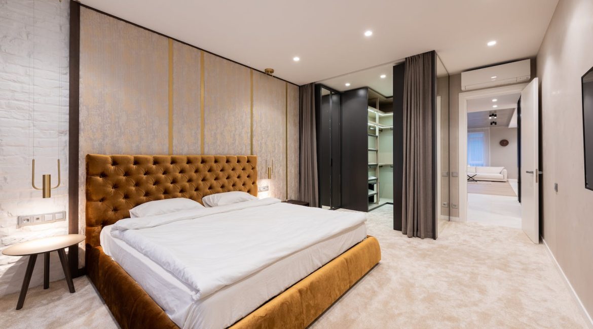 Interior of light spacious apartment with bed and table near wardrobe with curtains and door to living room