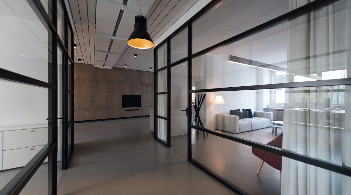 Modern open-plan interior with glass partitions, showing a living area with a sofa and minimalistic décor