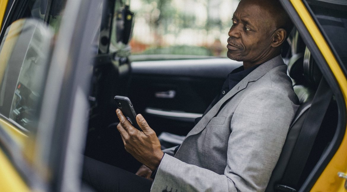 Contemplative black businessman using smartphone in taxi
