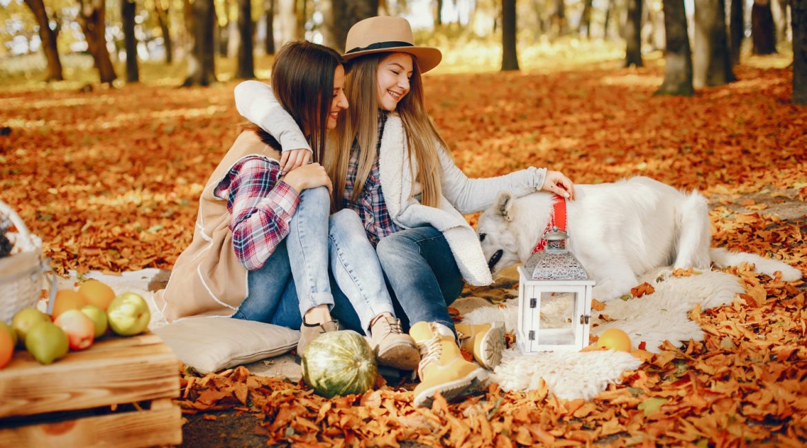 Two young women sitting on the ground surrounded by colorful autumn leaves in a serene outdoor setting
